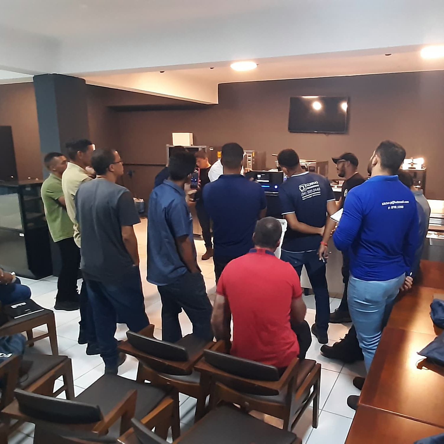 Um grupo de homens está reunido em uma sala com um homem vestindo uma camisa vermelha que diz jesus