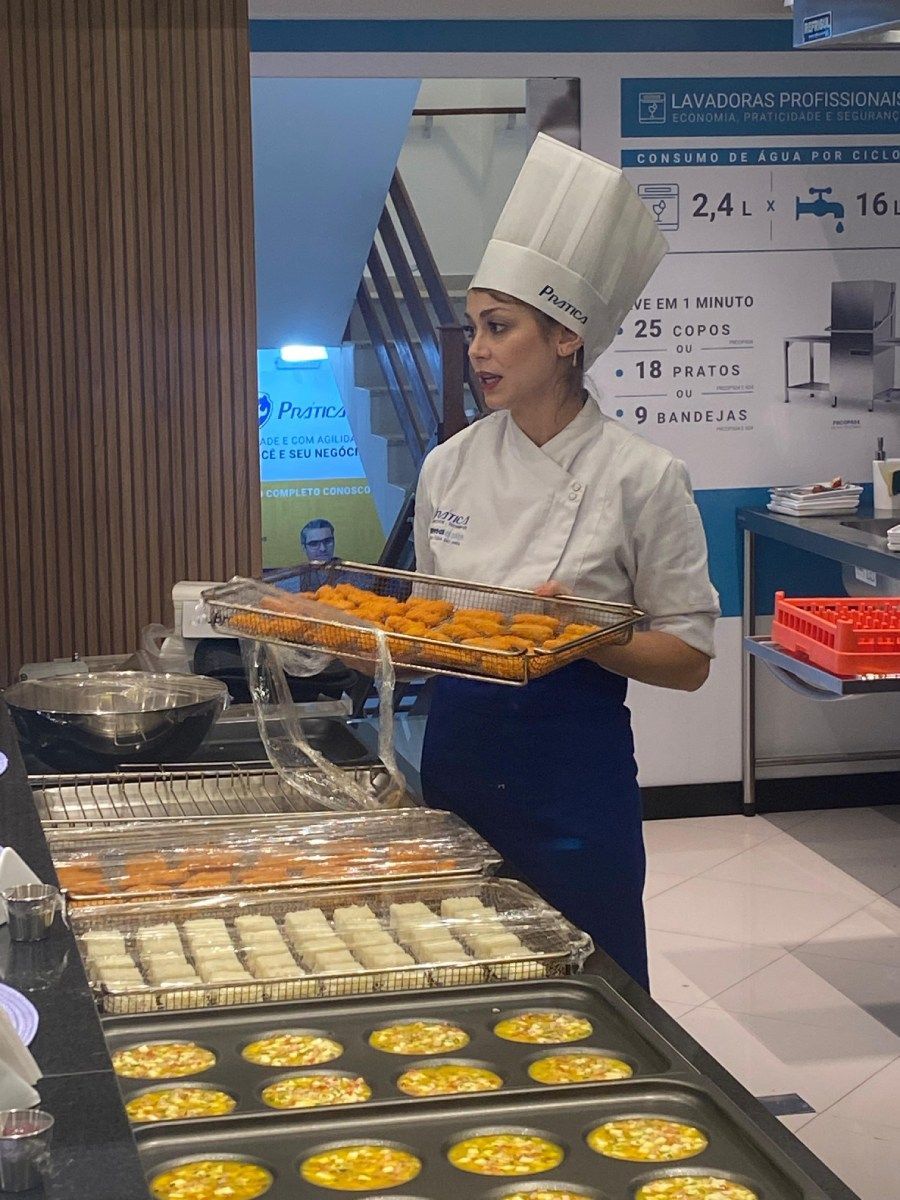 Uma mulher com chapéu de chef segura uma bandeja de comida