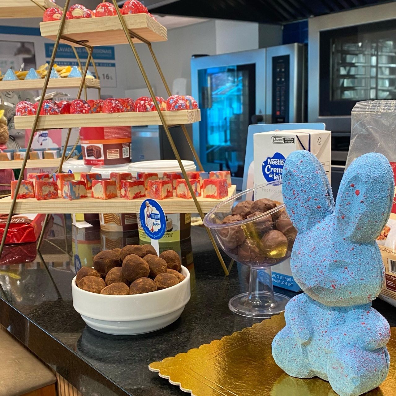 Um coelho azul está sentado em uma mesa ao lado de uma tigela de chocolates