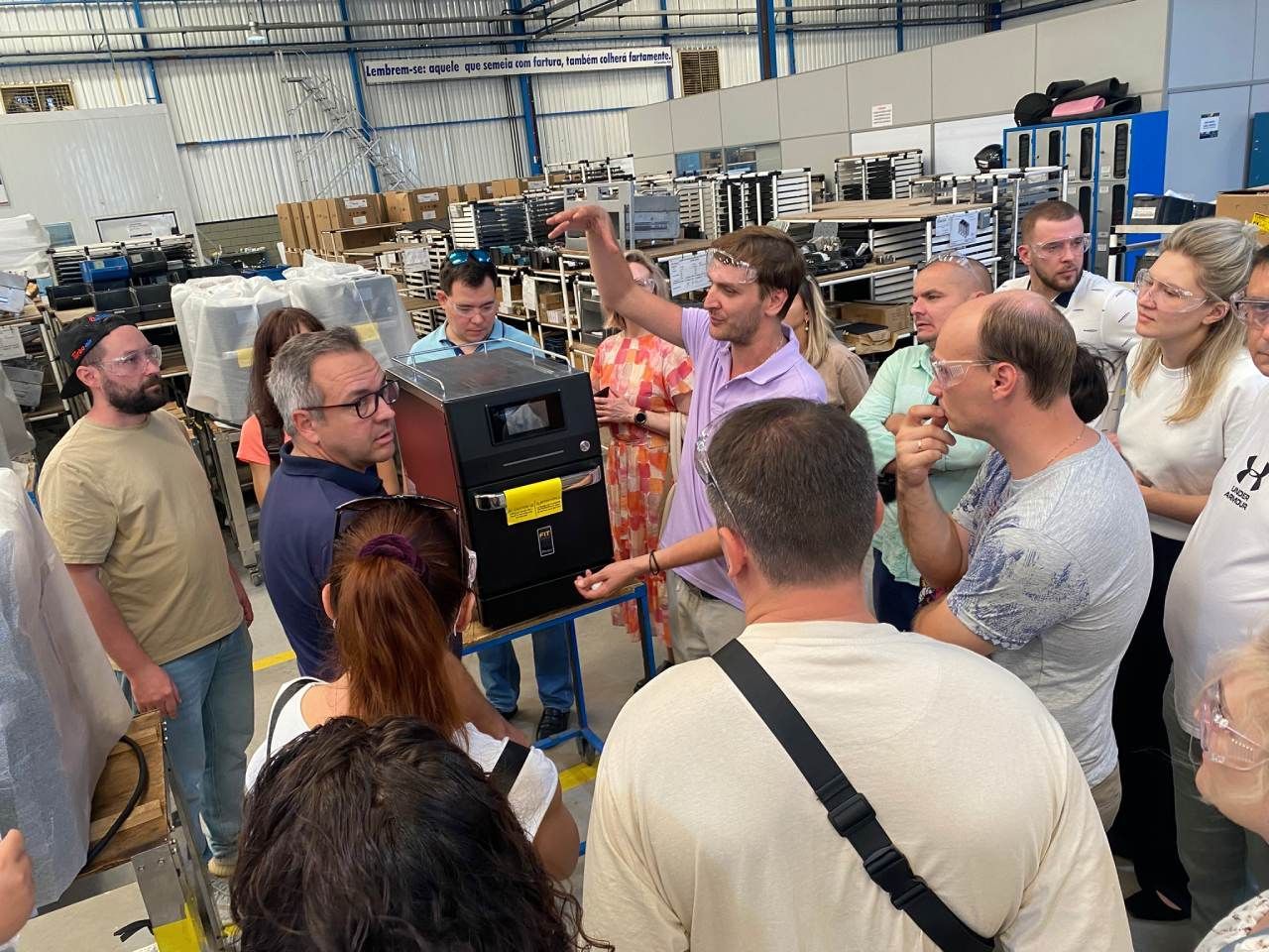 Um grupo de pessoas está em volta de uma máquina em um armazém.