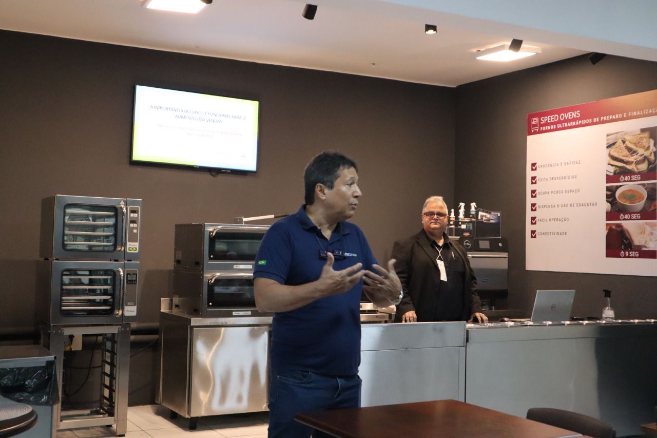 Um homem de camisa azul está fazendo uma apresentação em uma cozinha.