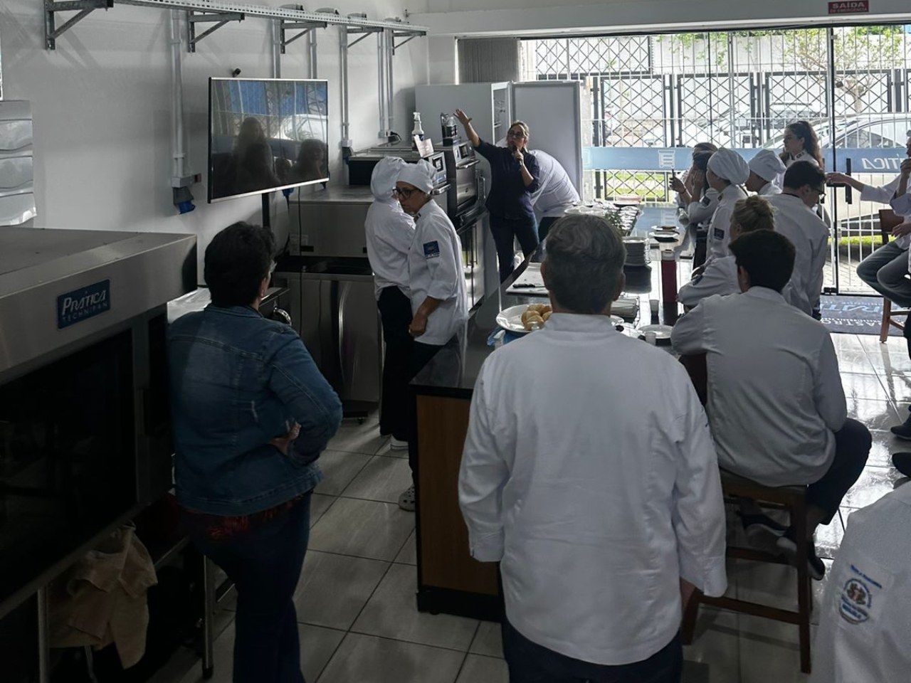 Um grupo de pessoas está em uma cozinha observando um chef