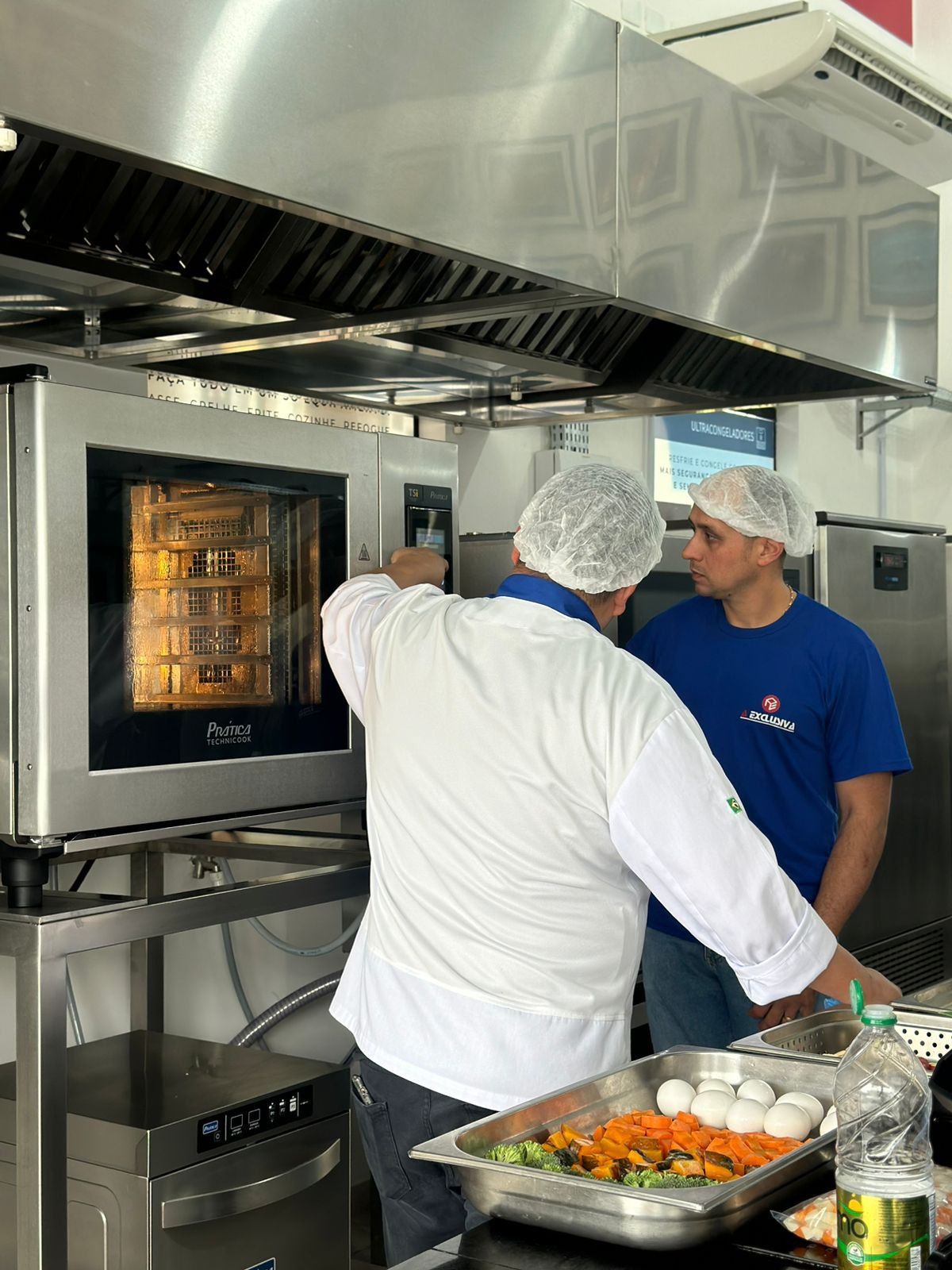 Um homem de camisa azul está conversando com um homem de camisa branca na cozinha.