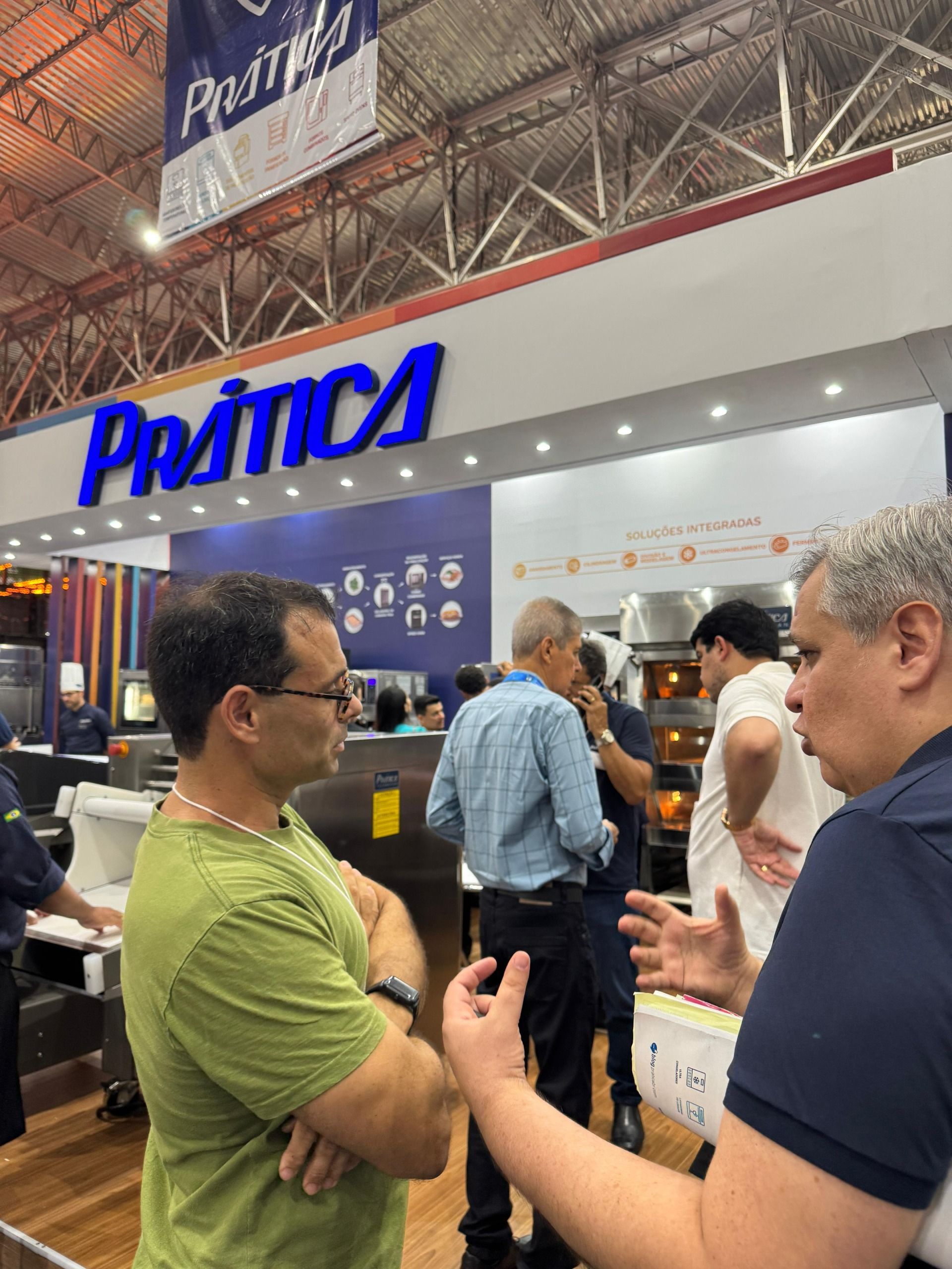 Dois homens conversando em frente a uma placa azul com a palavra 