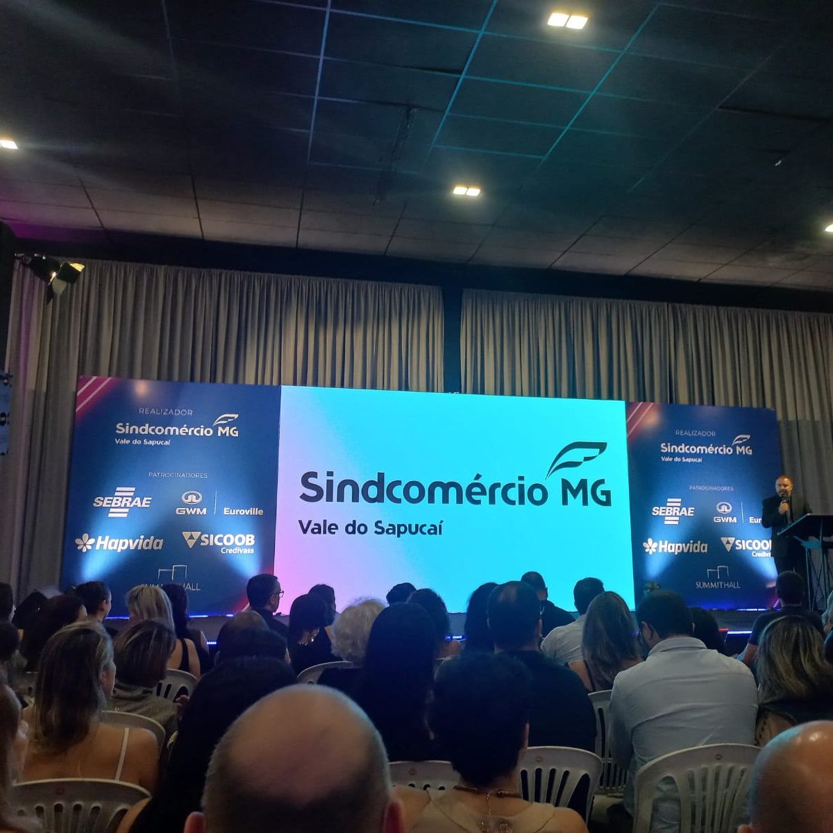 Um grupo de pessoas sentadas em frente a uma tela que diz sindcomercio mg