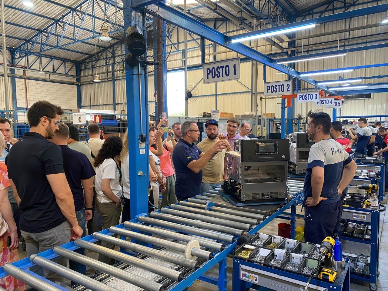 Um grupo de pessoas está em pé ao redor de uma correia transportadora em uma fábrica.