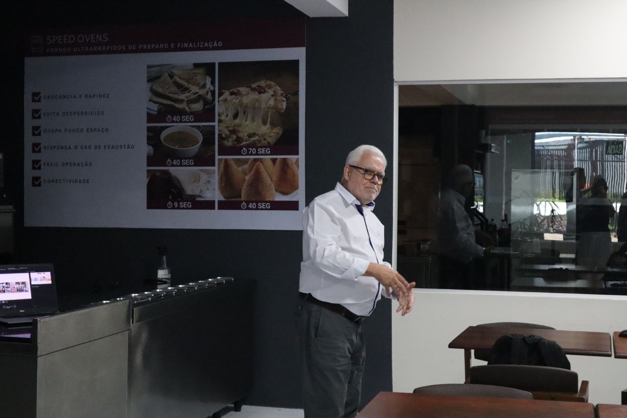 Um homem está fazendo uma apresentação em frente a uma parede com fotos de comida.
