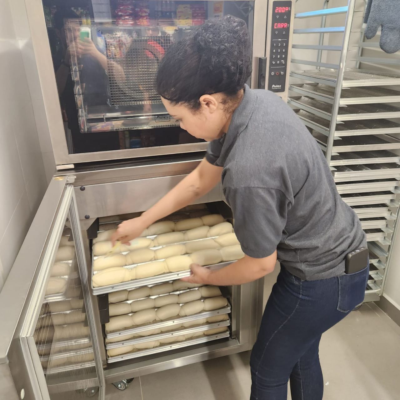 Uma mulher de camisa cinza está colocando comida no forno
