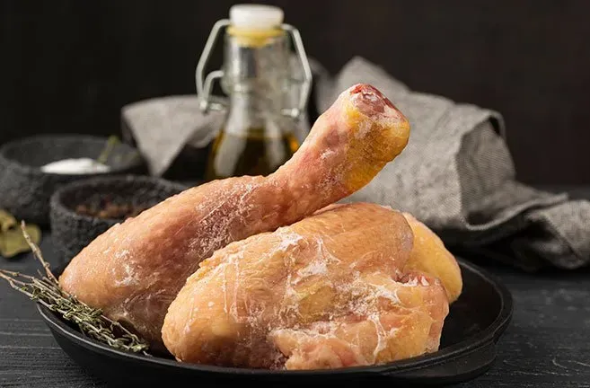 Duas coxas de frango congeladas em um prato preto sobre uma mesa.