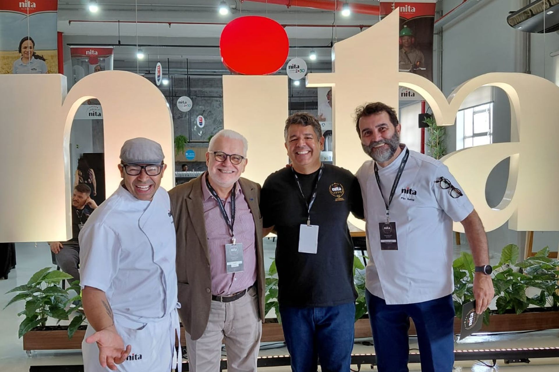 Quatro pessoas sorriem em frente a uma grande placa cor creme com a palavra 