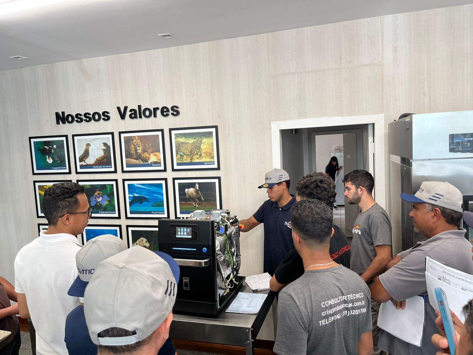 Um grupo de pessoas está em pé ao redor de uma máquina em frente a uma parede com fotos.
