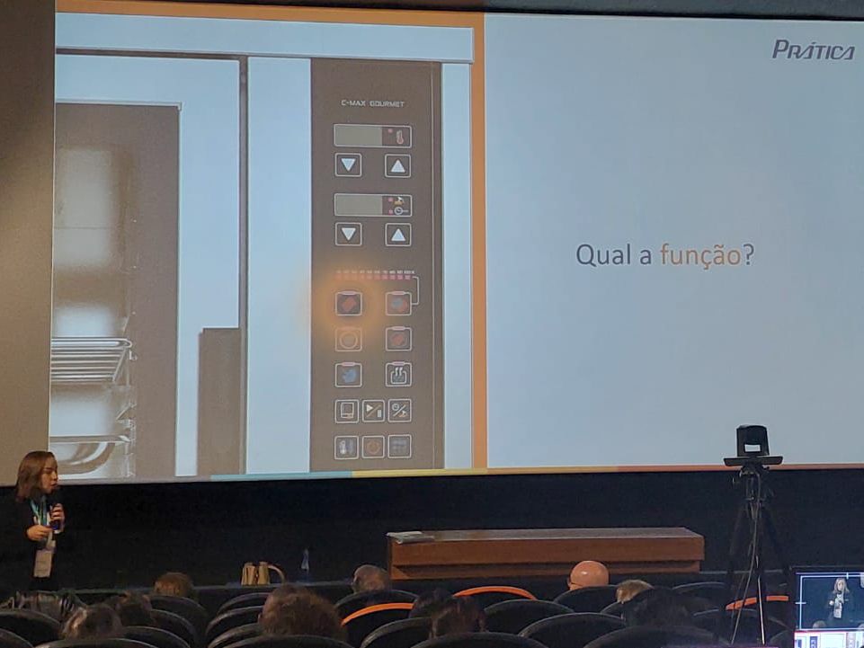 Uma mulher está fazendo uma apresentação em frente a uma tela grande que diz qual a funcao