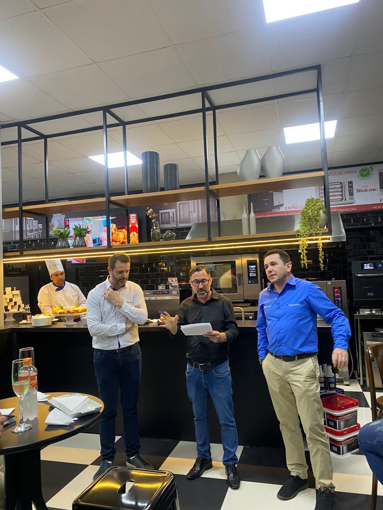 Um grupo de homens está em uma cozinha conversando entre si.