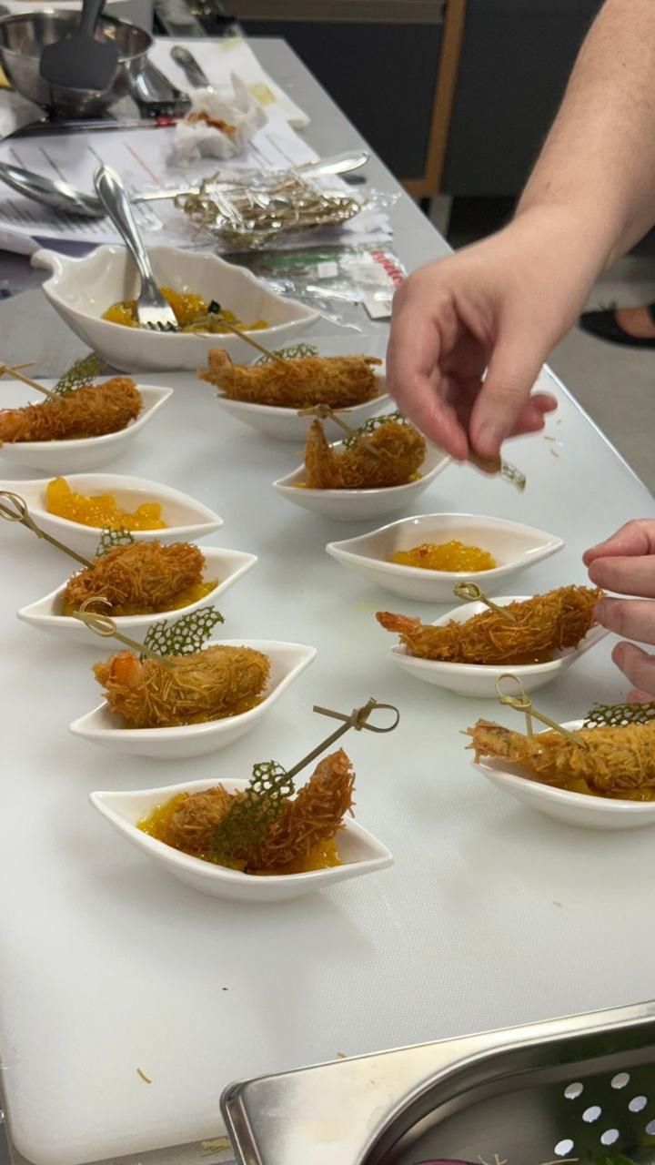 Um chef serve aperitivos de camarão frito em pratos brancos, sobre uma tábua de corte branca.