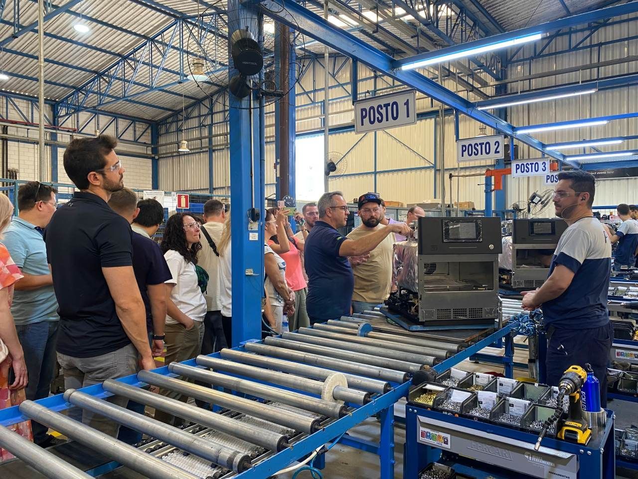 Um grupo de pessoas está em pé ao redor de uma correia transportadora em uma fábrica.