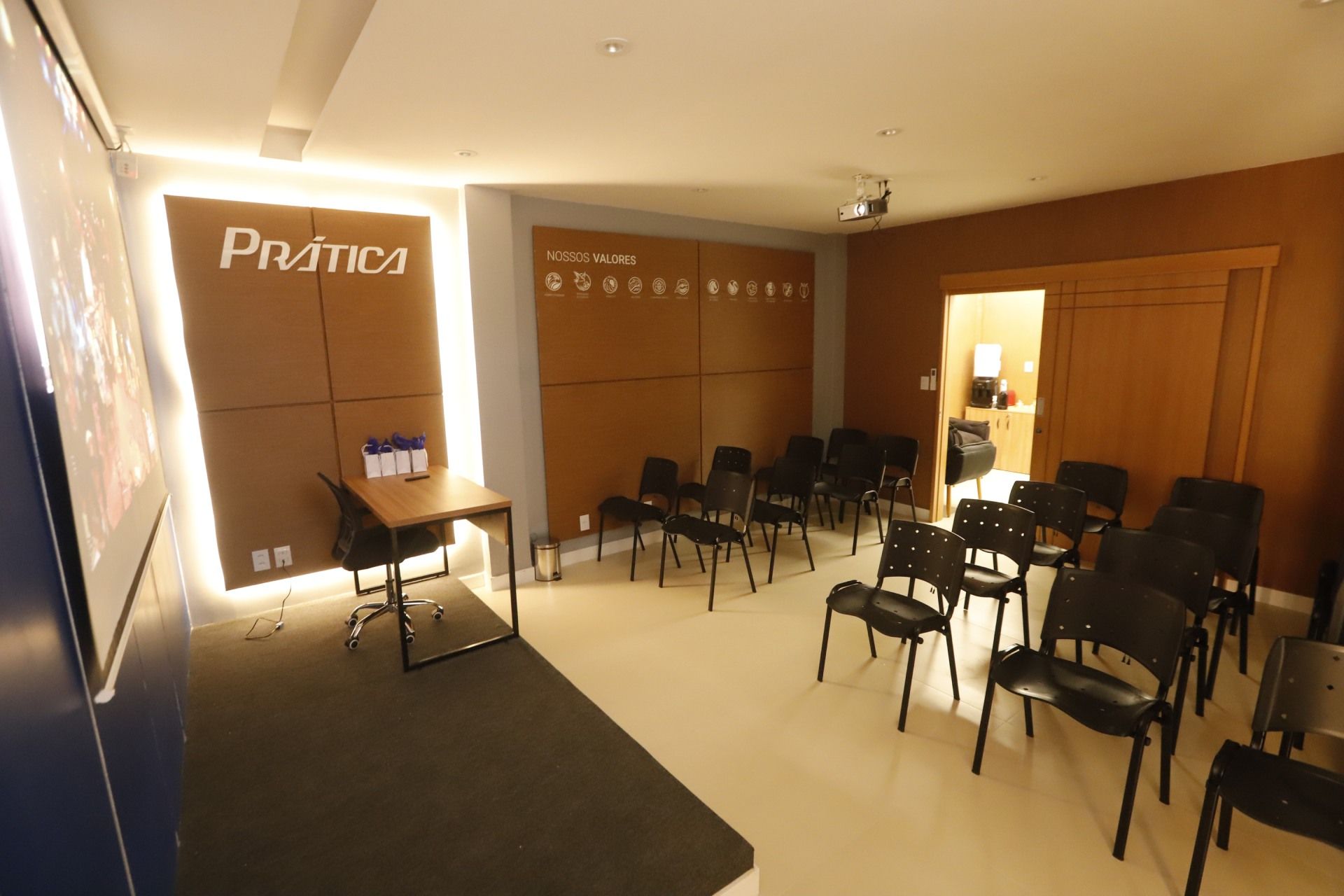 Uma sala de conferências vazia com cadeiras, uma tela de projetor e uma pequena mesa com suprimentos.