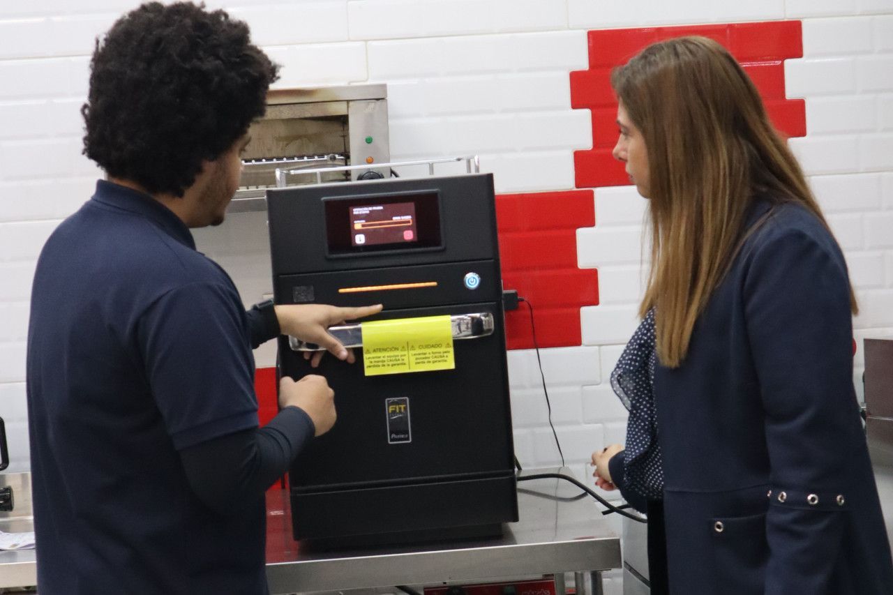 Um homem e uma mulher estão em frente a uma máquina que tem uma placa amarela