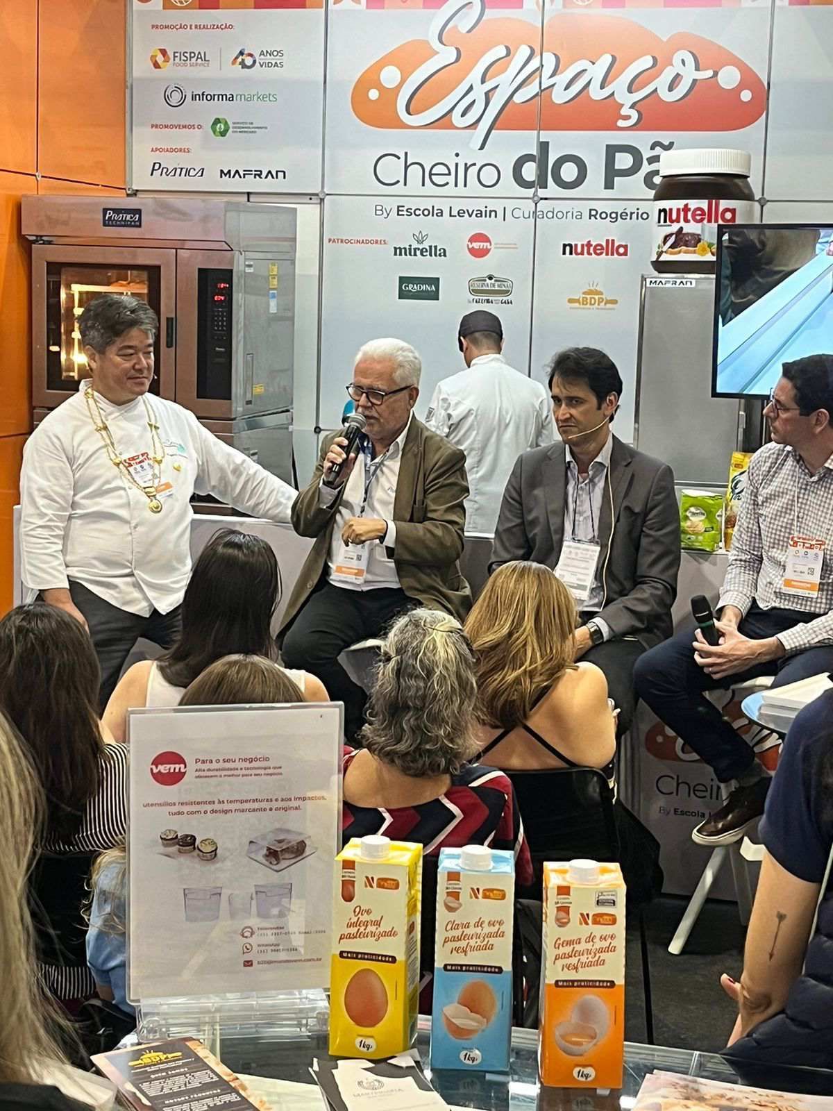 Um grupo de pessoas está sentado em frente a um microfone em uma sala.