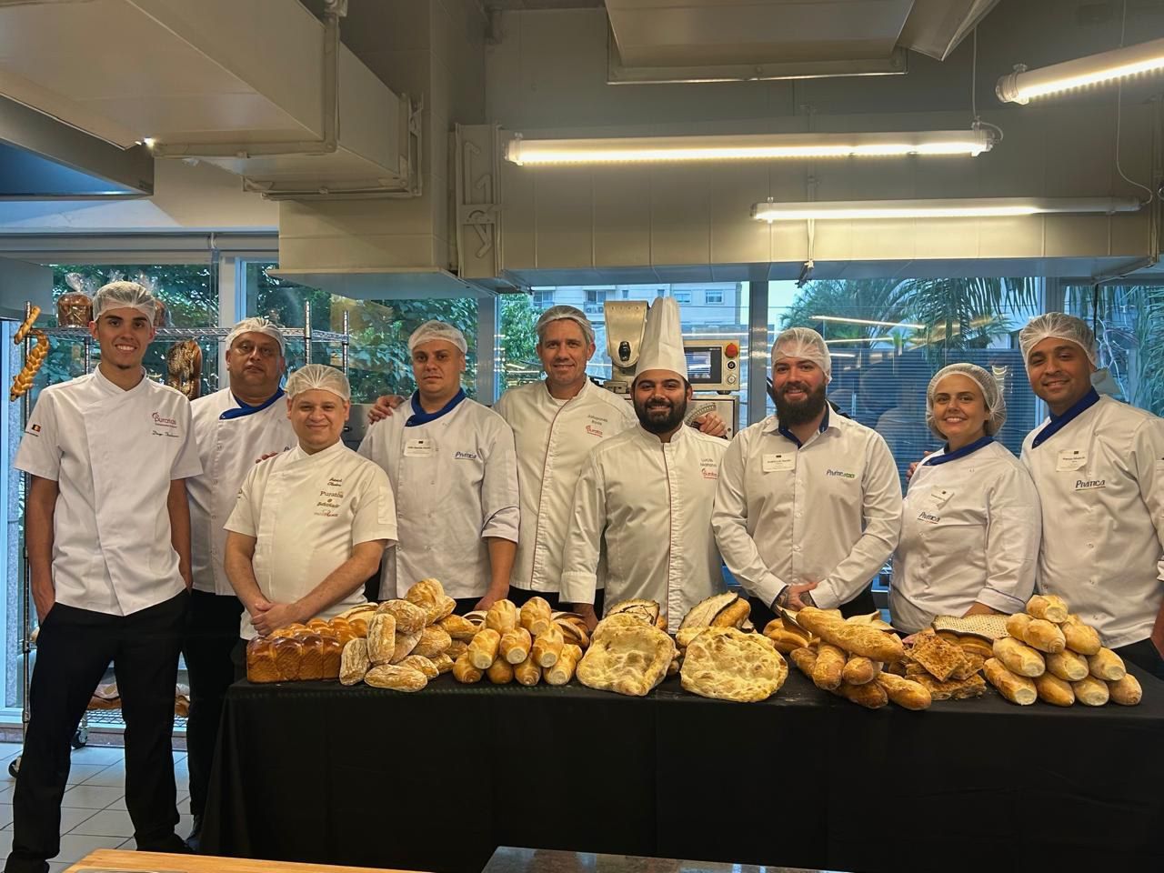Um grupo de chefs está posando para uma foto em frente a uma mesa cheia de pão.