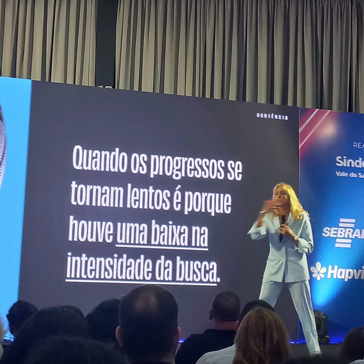 A woman stands in front of a screen that says quando os progressos se tornam lentos