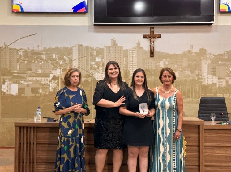 Um grupo de mulheres estão de pé, uma ao lado da outra, em uma sala com uma cruz na parede.