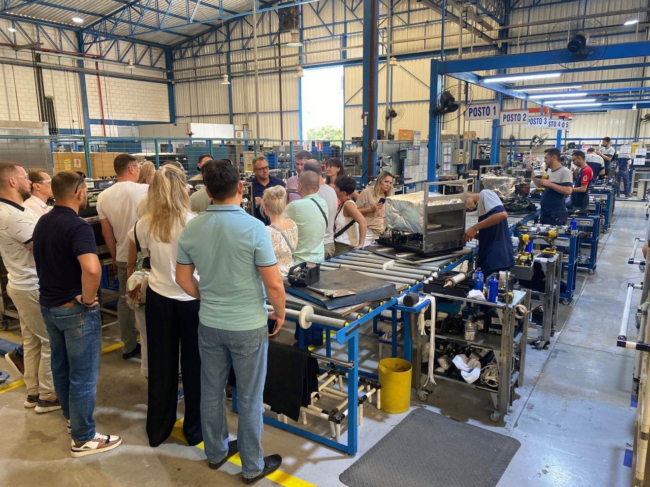 Um grupo de pessoas está em uma fábrica olhando para uma máquina.