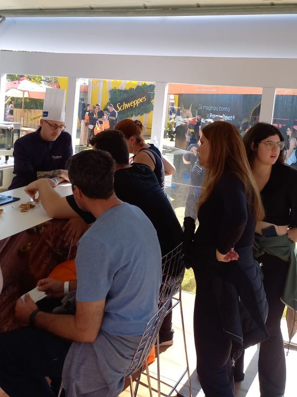 Um grupo de pessoas sentadas em uma mesa com uma placa de schweppes ao fundo