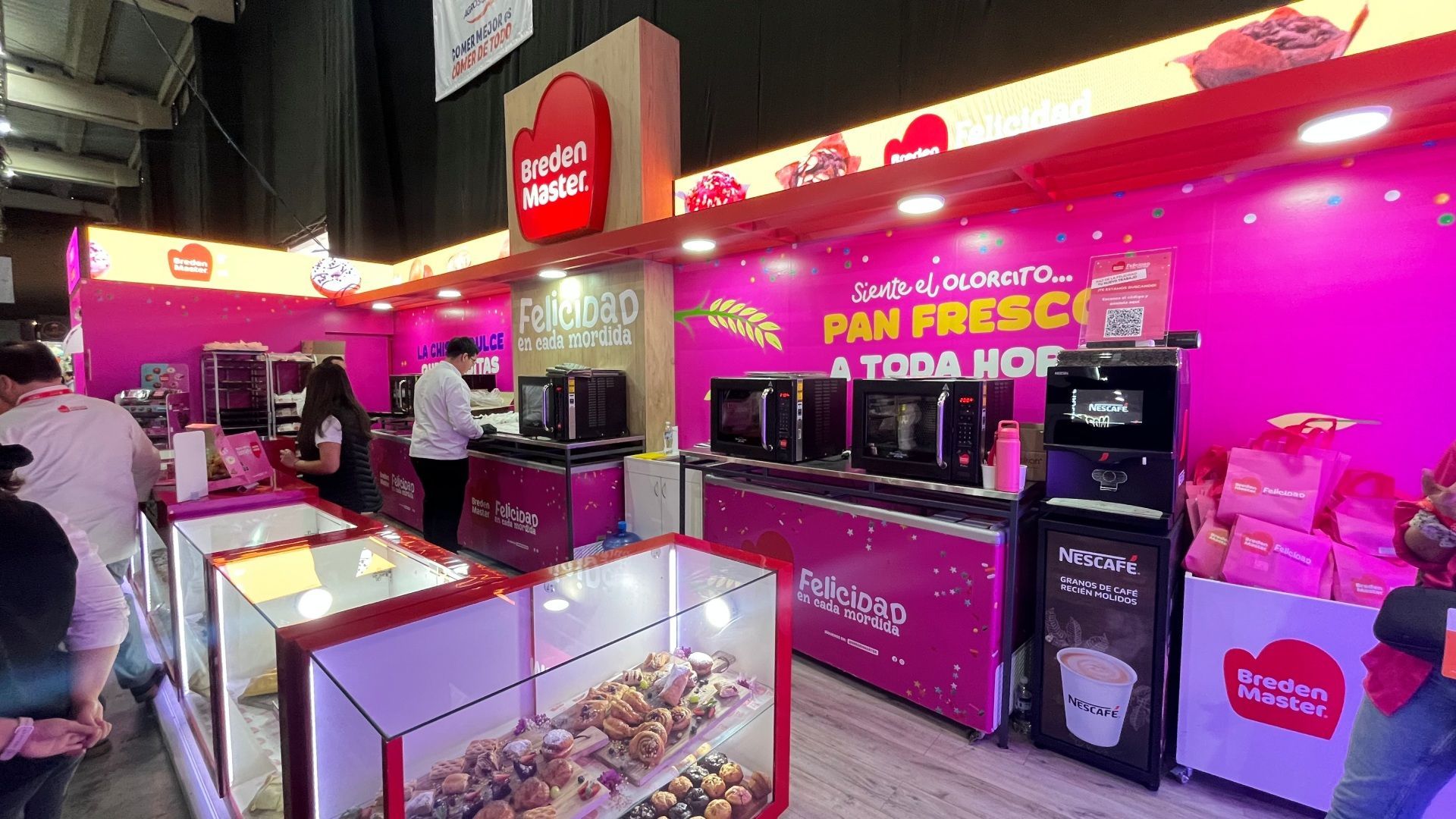 Um estande rosa de uma padaria em uma feira. Produtos assados ​​em vitrines, fornos e funcionários presentes.