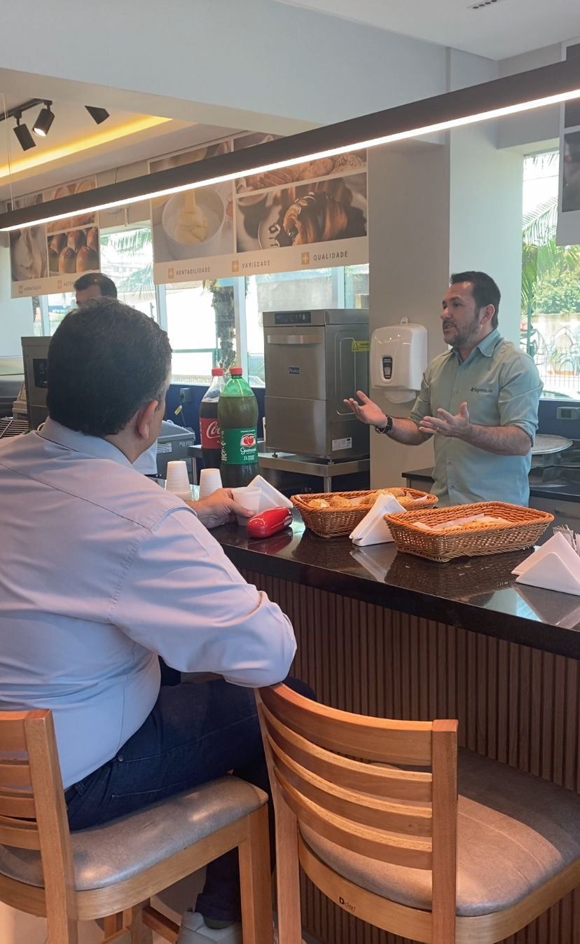 Um homem está sentado à mesa de um restaurante conversando com outro homem.