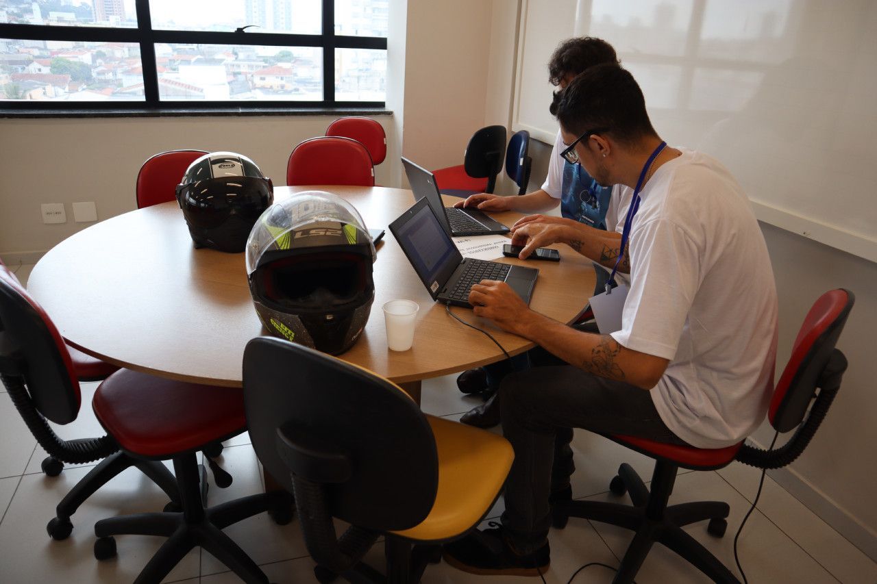 Um grupo de pessoas está sentado ao redor de uma mesa usando laptops