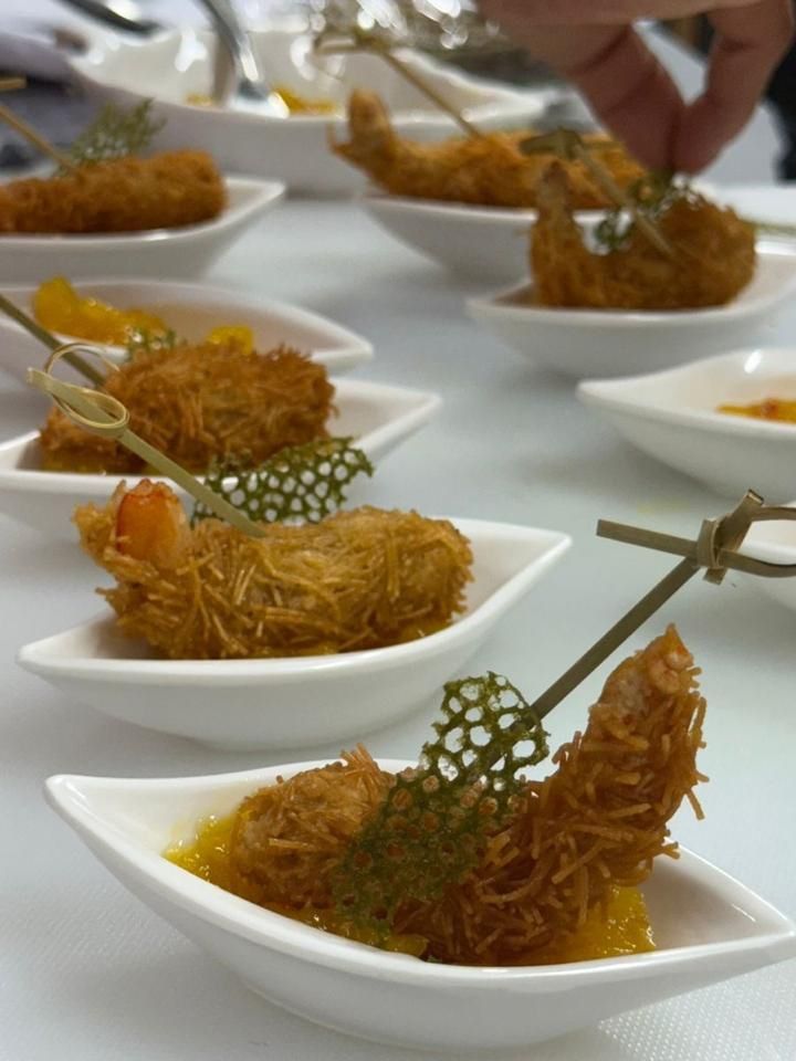 Aperitivos de camarão frito em pequenos pratos brancos, guarnecidos com ervas.