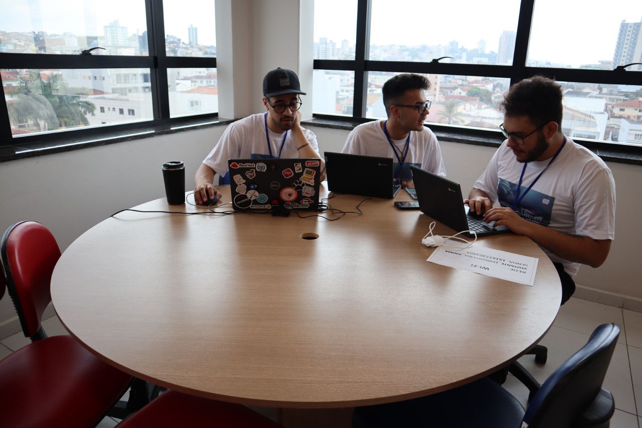 Três homens estão sentados em uma mesa redonda com laptops.