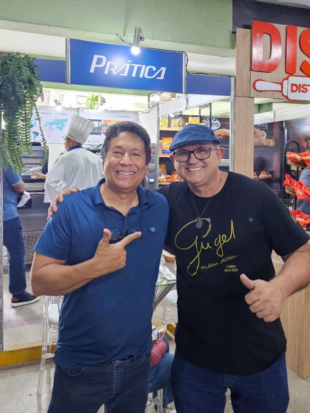 Dois homens estão posando para uma foto em frente a uma placa que diz practica
