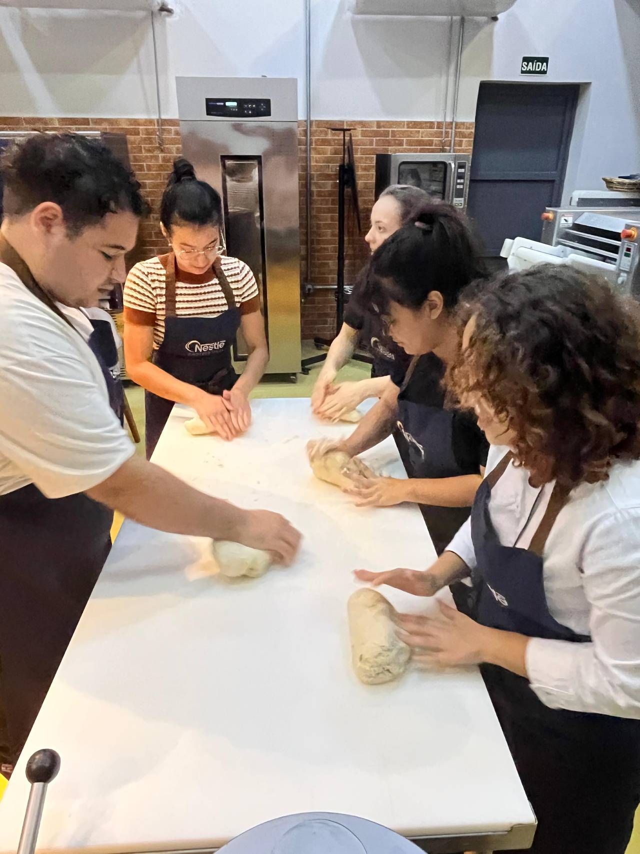 Um grupo de pessoas está amassando massa em uma mesa na cozinha.
