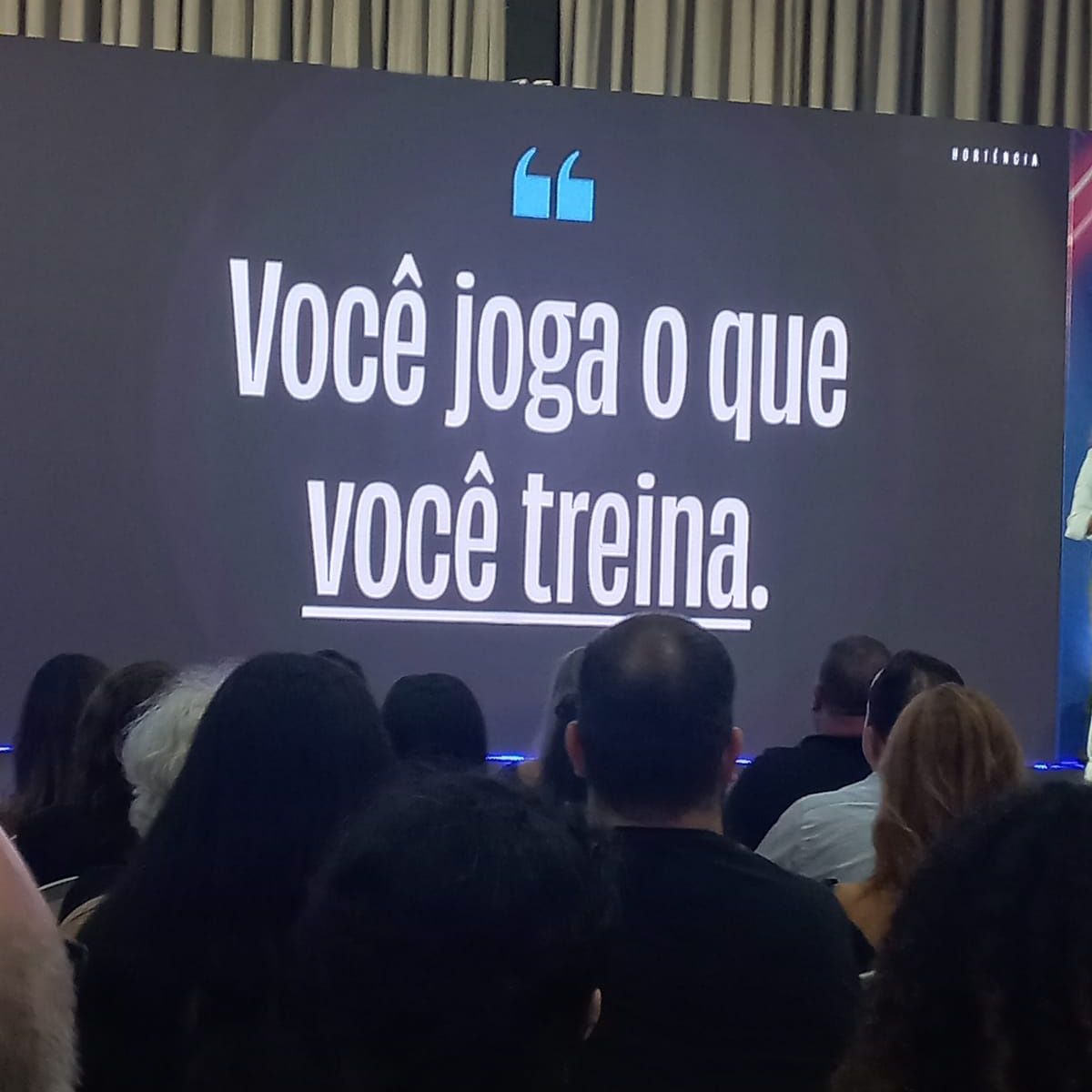 A group of people sitting in front of a screen that says voce joga o que voce treina