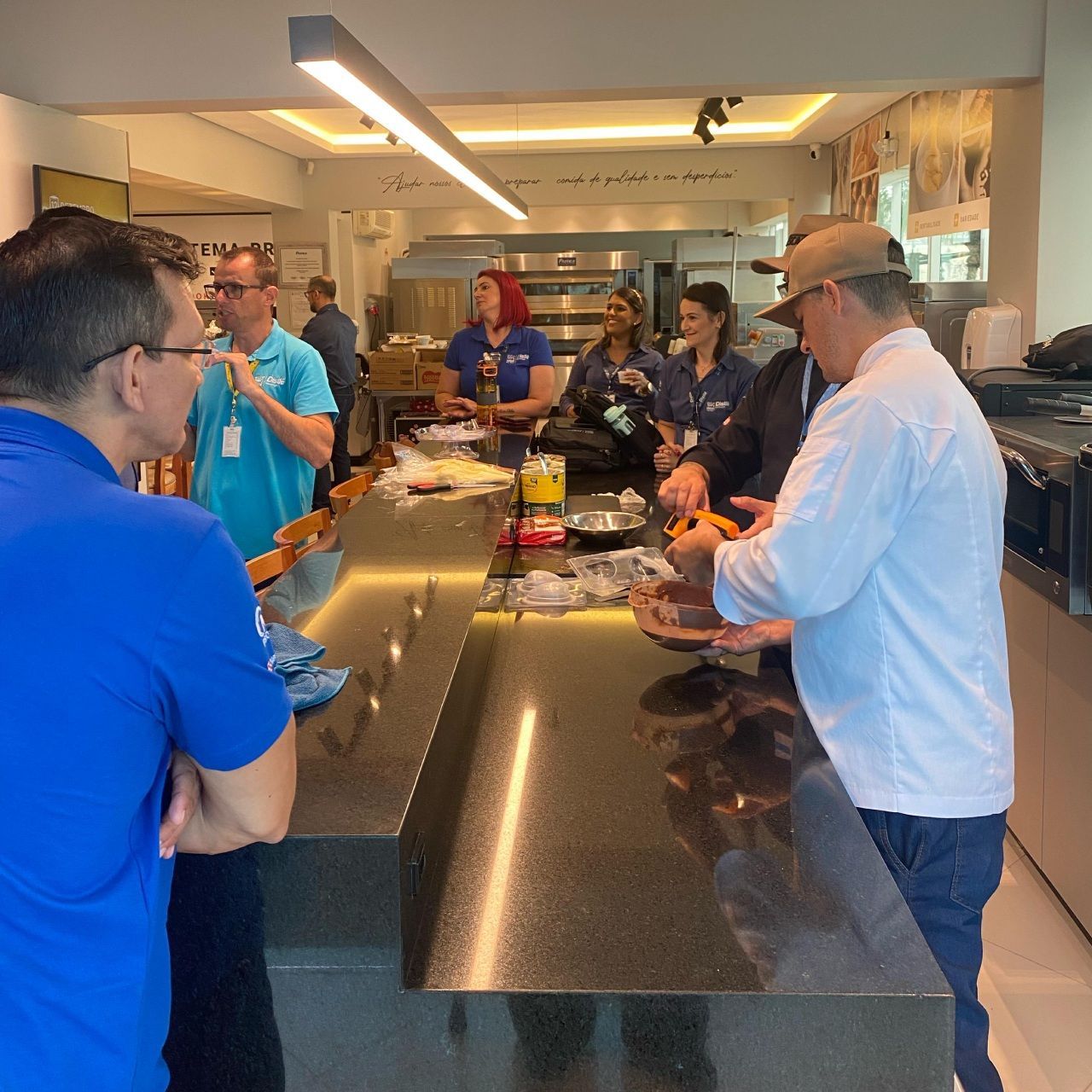 Um grupo de pessoas em pé ao redor de um balcão em uma cozinha