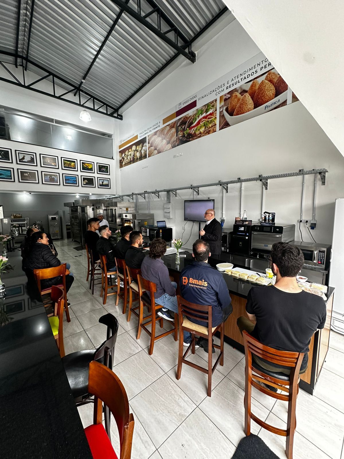 Um grupo de pessoas está sentado em cadeiras em uma sala com um homem fazendo uma apresentação.
