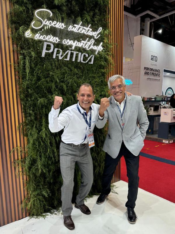 Dois homens estão posando para uma foto em frente a uma parede verde.