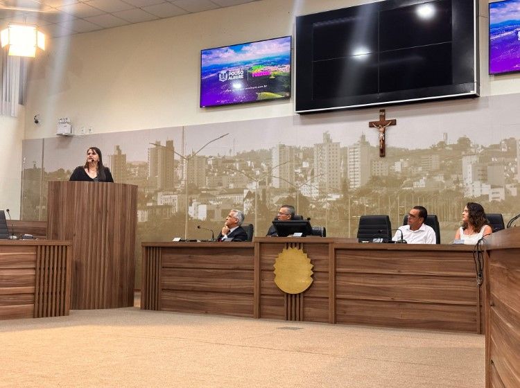 Uma mulher está de pé em um pódio em uma sala com pessoas sentadas em mesas.