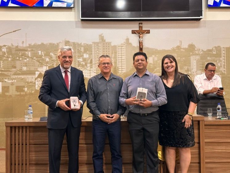 Um grupo de pessoas está posando para uma foto em uma sala com uma cruz na parede.