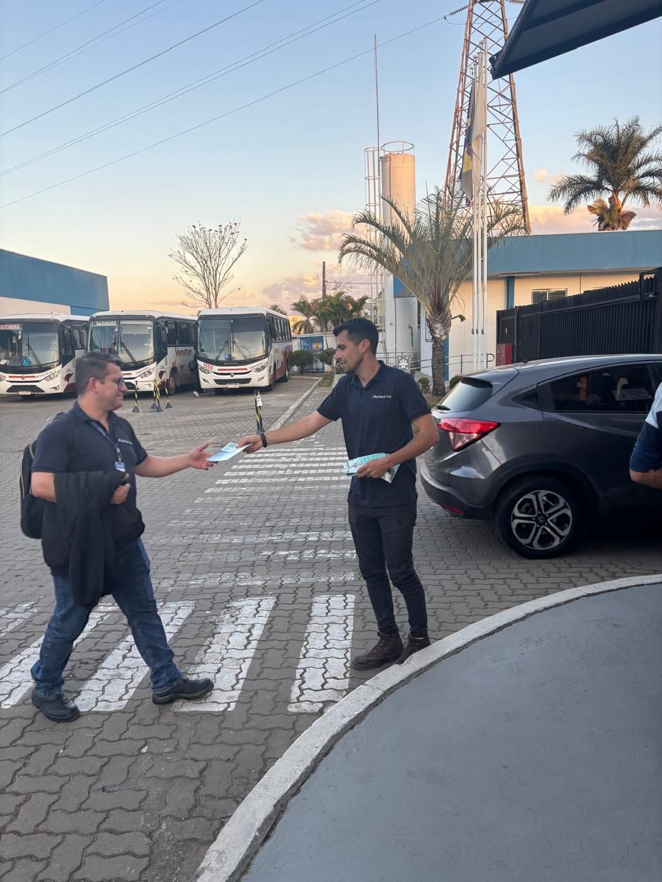 Dois homens estão parados em um estacionamento entregando panfletos um ao outro
