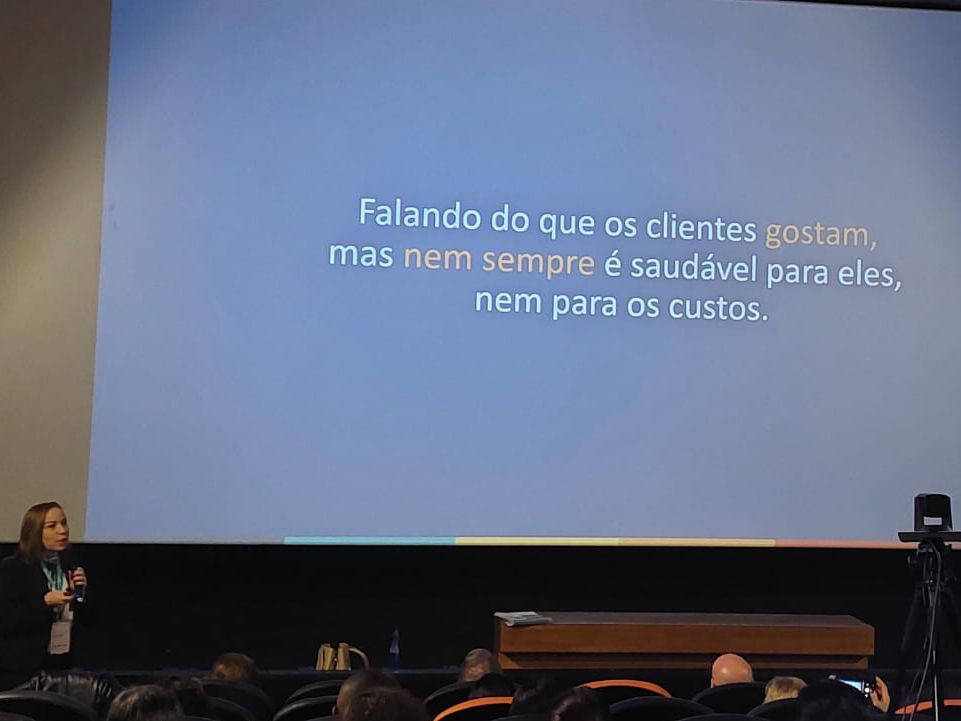 Uma mulher está fazendo uma apresentação em frente a uma tela grande.