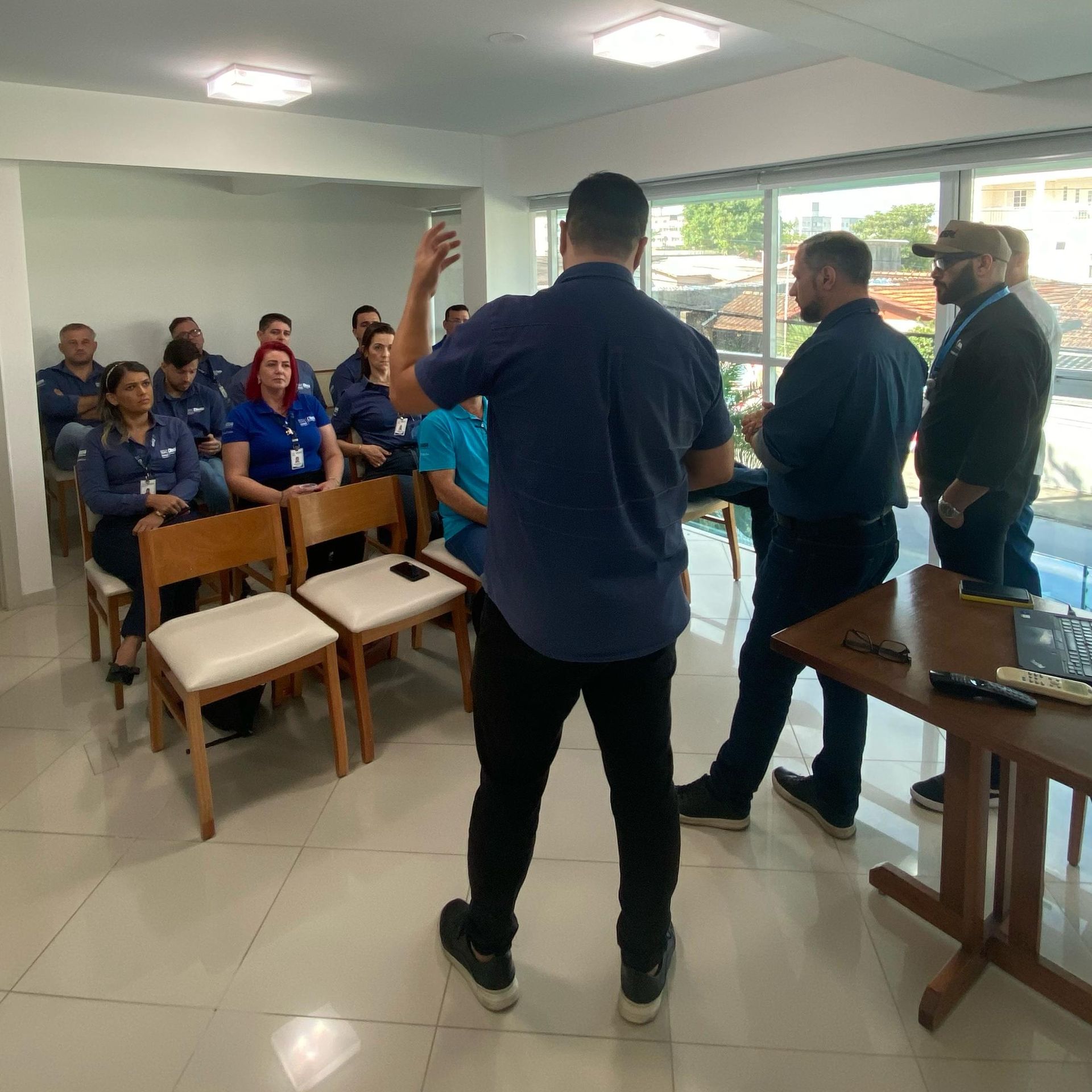 Um homem está de pé na frente de um grupo de pessoas sentadas em cadeiras.