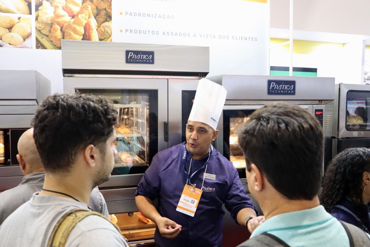 Um homem com chapéu de chef está conversando com um grupo de pessoas.