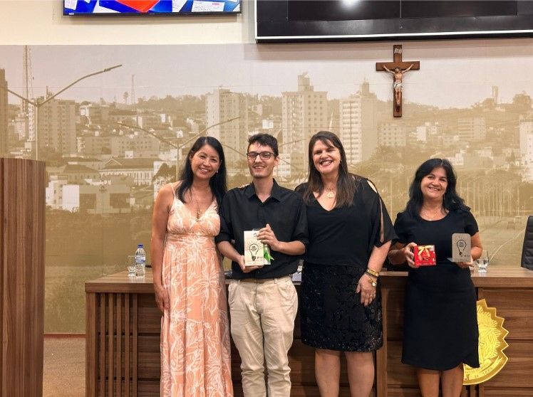 Um grupo de pessoas está de pé, uma ao lado da outra, em uma sala com uma cruz na parede.