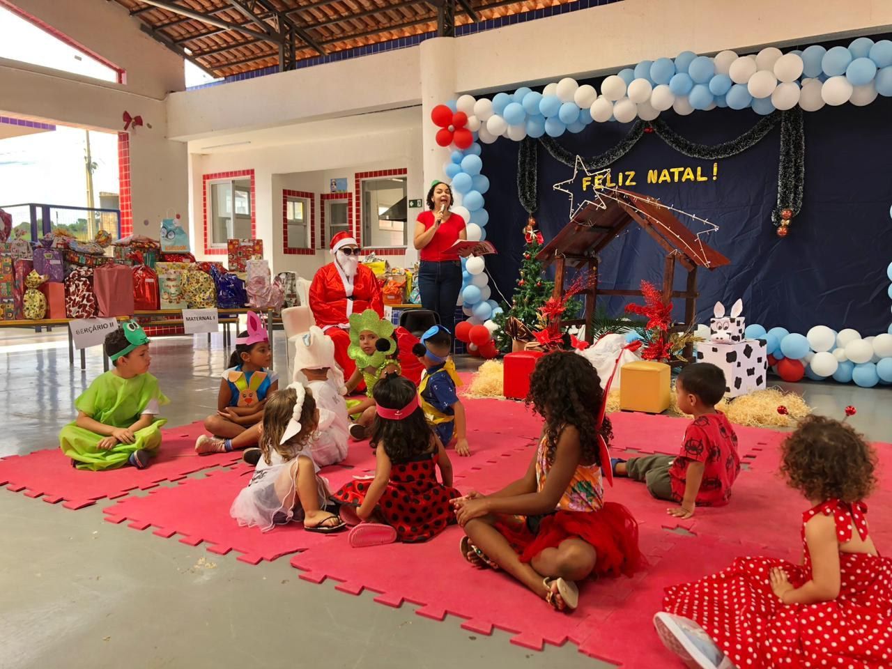 Um grupo de crianças está sentado no chão em uma sala decorada para o natal.