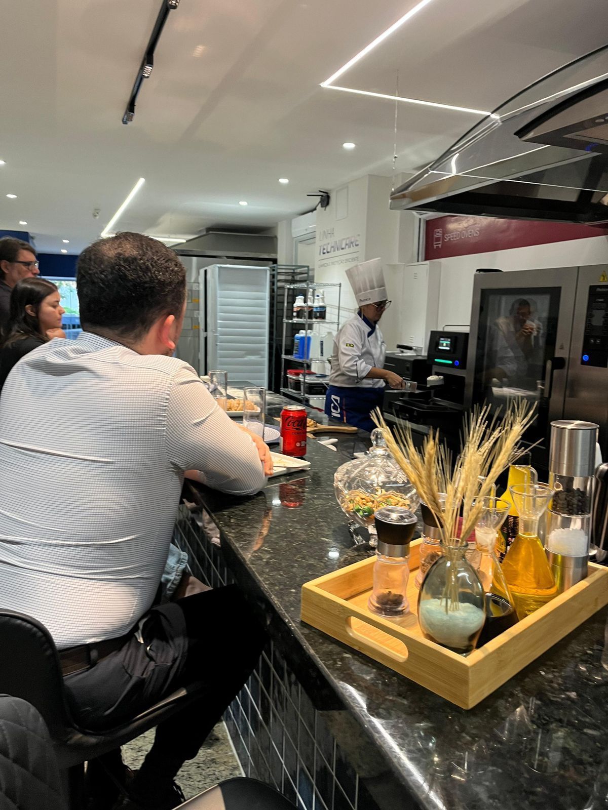 Pessoas em um bar observam um chef cozinhando atrás do balcão de um restaurante.