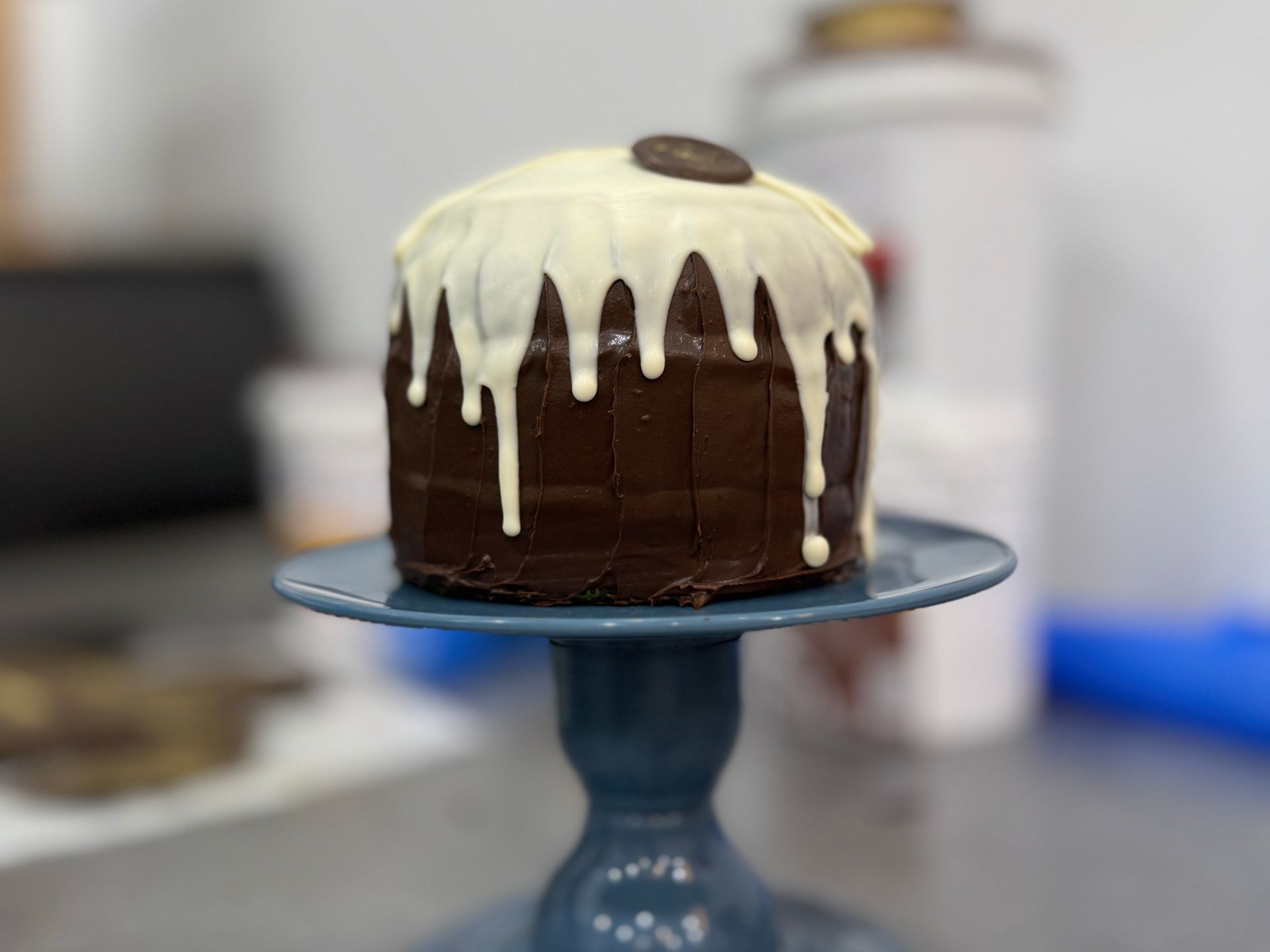 Bolo de chocolate com cobertura de chocolate branco servido em um suporte azul.