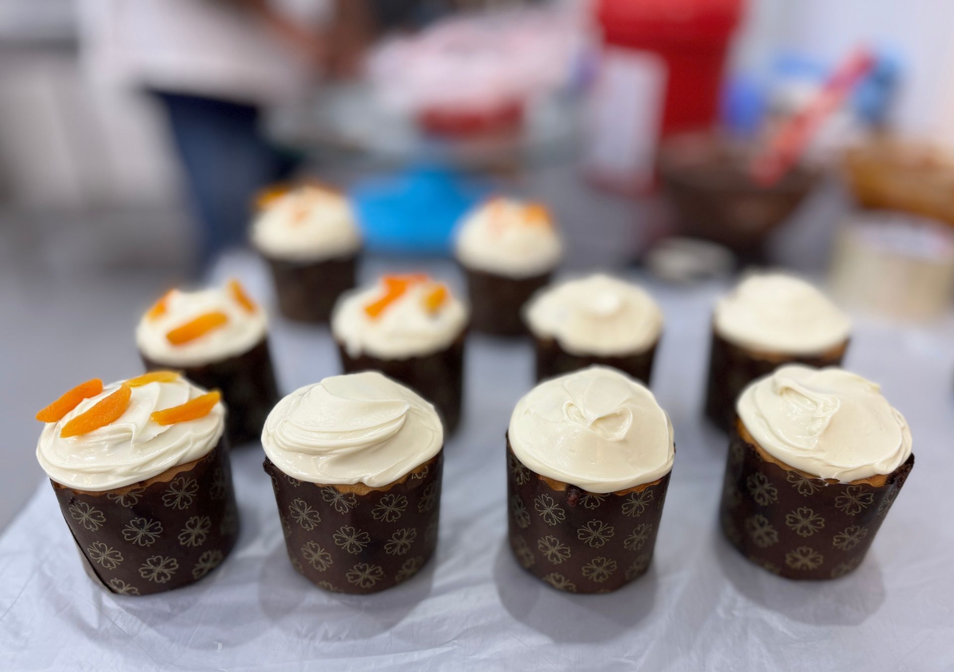 Cupcakes com cobertura branca e alguns com cobertura de frutas cítricas em uma mesa.