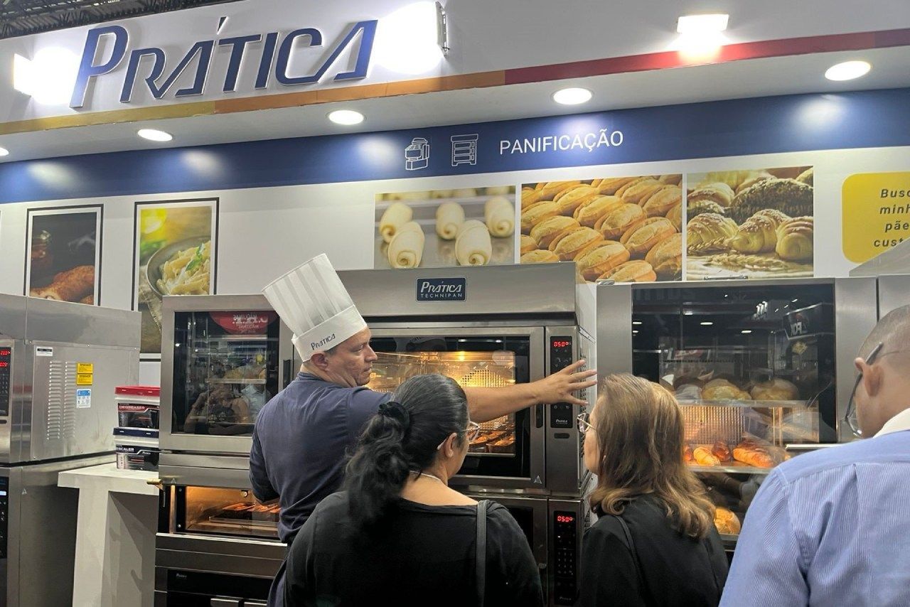 Um homem com chapéu de chef está ensinando um grupo de pessoas a usar um forno.